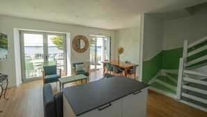 Una cocina moderna con encimera negra, un comedor con mesa y sillas de madera, y vista al mar a través de amplios ventanales correderas.