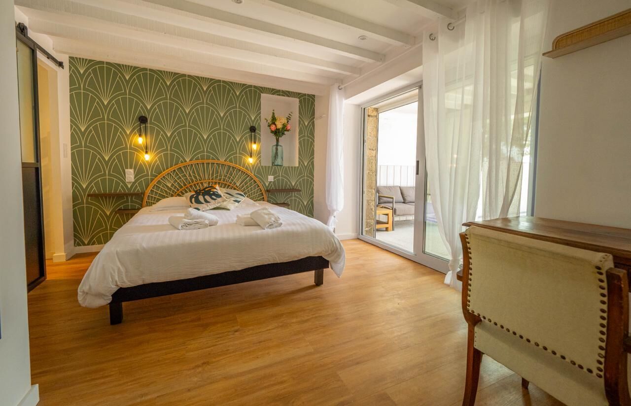 Ein Schlafzimmer mit einem Bett, Holzboden, Wand mit grünem Muster und einem Fenster mit Blick.