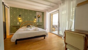 Un dormitorio con cama, suelo de madera, pared verde estampada y ventana con vistas.