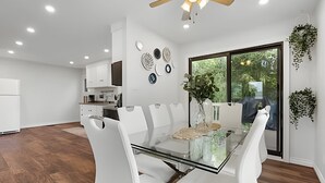 A modern kitchen with white cabinets, a dining area with a glass table and white chairs, and a ceiling fan. - Doran Farm & Wedding Venue (Richmond Hill)