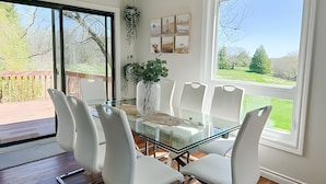 A dining area with a glass table and white chairs, a potted plant, and a view of a wooden deck and greenery. - Doran Farm & Wedding Venue (Richmond Hill)