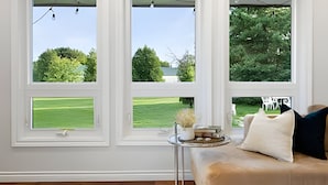 A room with three large windows, a sofa with cushions, a small table with a vase, and a view of a green lawn and trees. - Doran Farm & Wedding Venue (Richmond Hill)