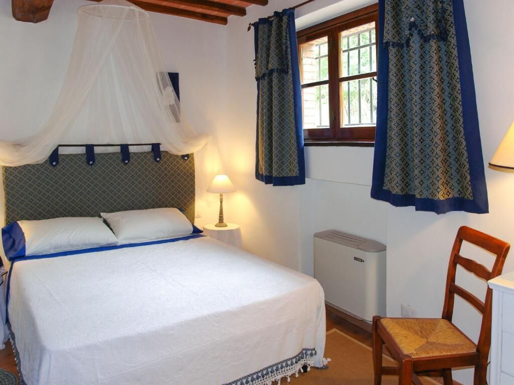 A bedroom with a bed, a bedside table, a lamp, a chair, and a window with curtains.