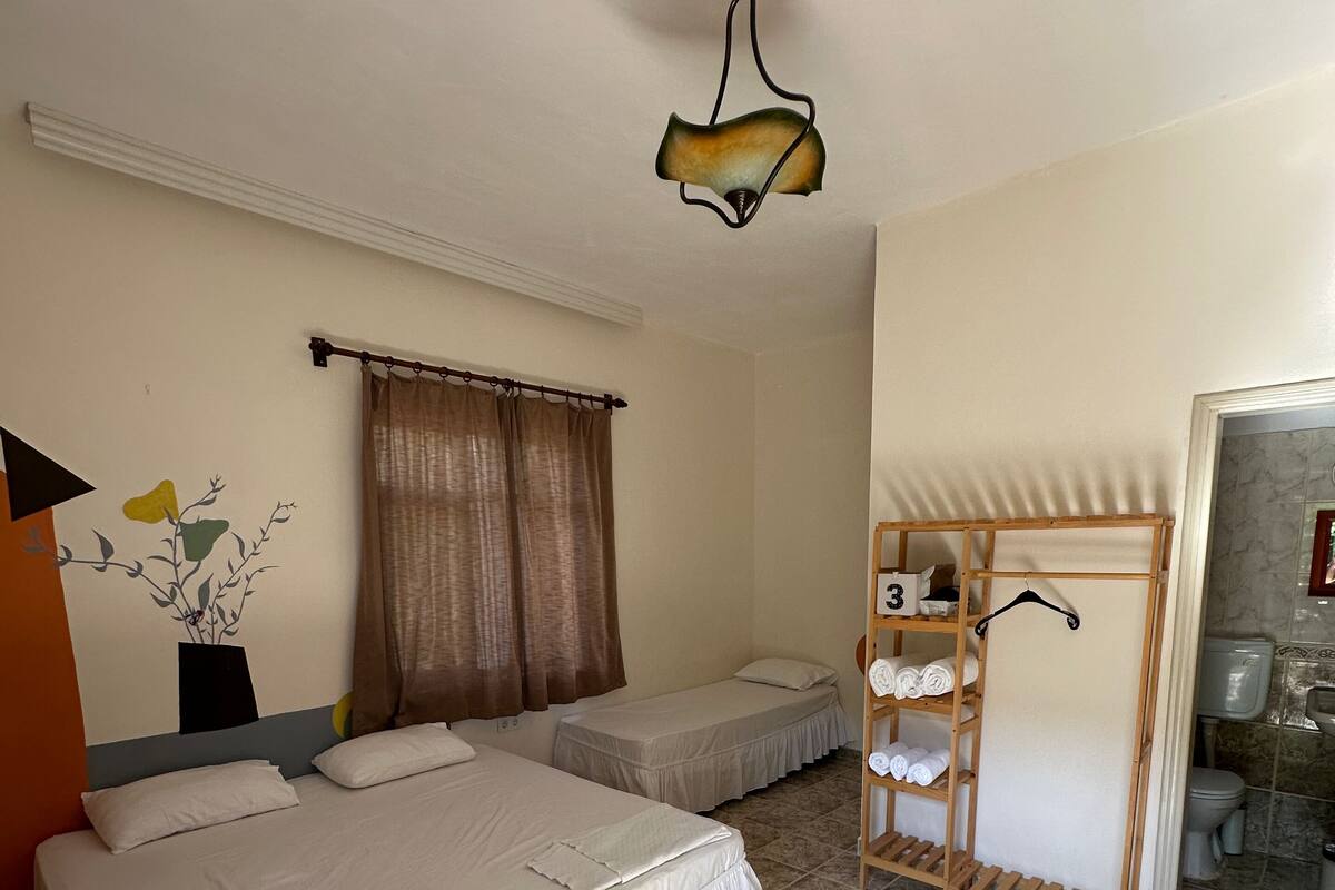 Een hotelkamer met twee bedden, een houten plank met handdoeken, een badkamer met toilet en wastafel, en een decoratief wandobject.