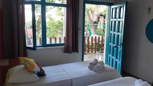 A room with two beds, a window with curtains, a blue door, and a wall with a circular design. - Gaya Pansiyon (Kemer)