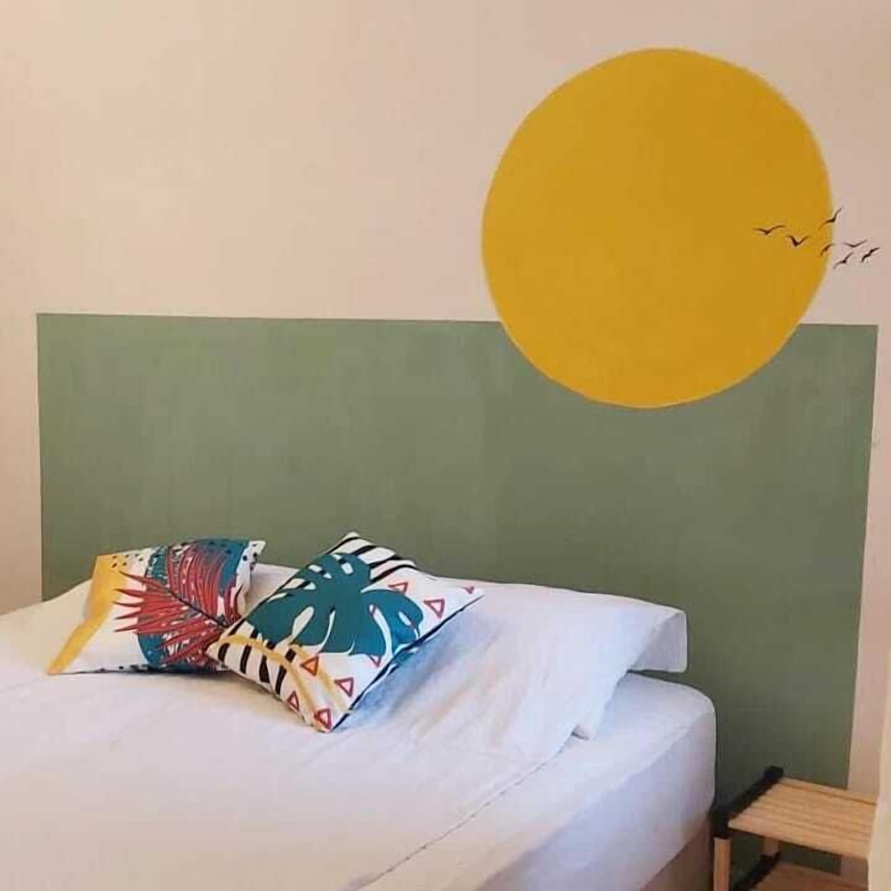 Un lit avec une literie blanche et des oreillers colorés, une tête de lit verte et un cercle jaune sur le mur.