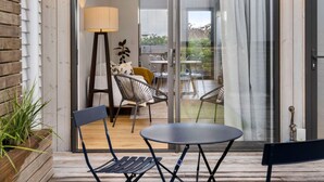 A modern outdoor seating area with a table and chairs, a lamp, and a view of the interior through a glass door.