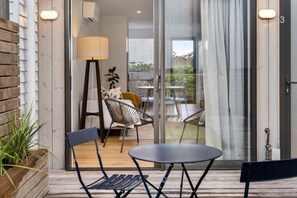 Ein moderner Außenbereich zum Sitzen mit Tisch und Stühlen, einer Lampe und Blick ins Innere durch eine Glastür.