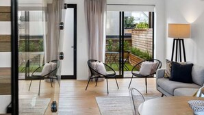 A modern living room with a sofa, chairs, a glass coffee table, and a view of the outdoors through large windows.