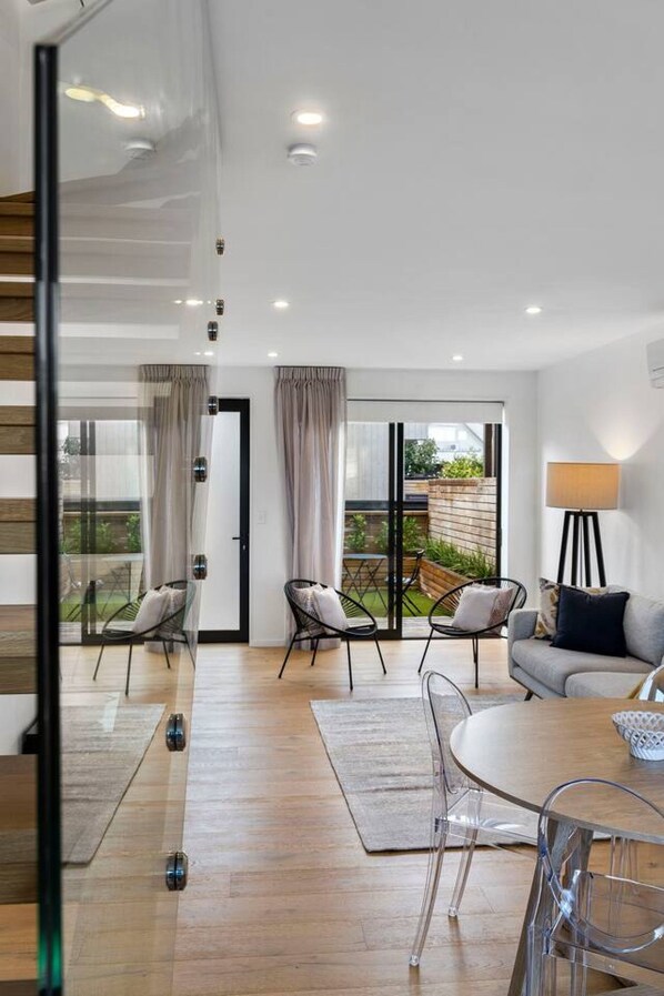 A modern living room with a sofa, chairs, a glass coffee table, and a view of the outdoors through large windows.