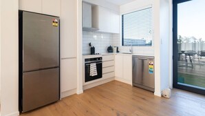 A modern kitchen with white cabinetry, a stainless steel refrigerator, a dishwasher, and a window with blinds.