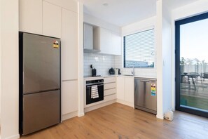 Eine moderne Küche mit weißen Schränken, einem Edelstahl-Kühlschrank, einer Spülmaschine und einem Fenster mit Jalousien.