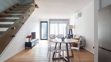 A modern kitchen with a built-in refrigerator, a dining area with a round table and chairs, and a staircase with wooden steps.
