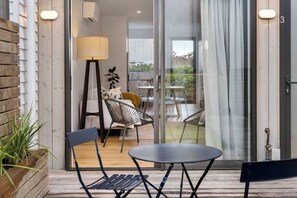 Un espacio exterior moderno con asientos, una mesa, sillas, una lámpara y vistas al interior de la casa.
