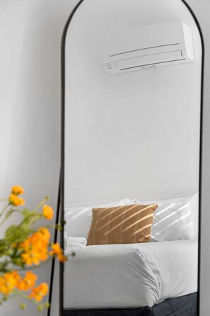 Ein Bett mit weißer Bettwäsche und einem braun gestreiften Kopfkissen, ein kleiner Nachttisch und eine an der Wand befestigte Klimaanlage.