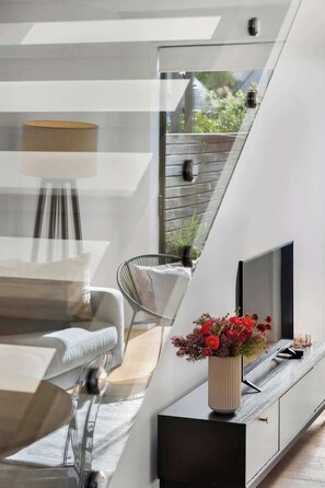 Un interior moderno con un sofá, una butaca, un televisor y una planta sobre una plataforma de madera.