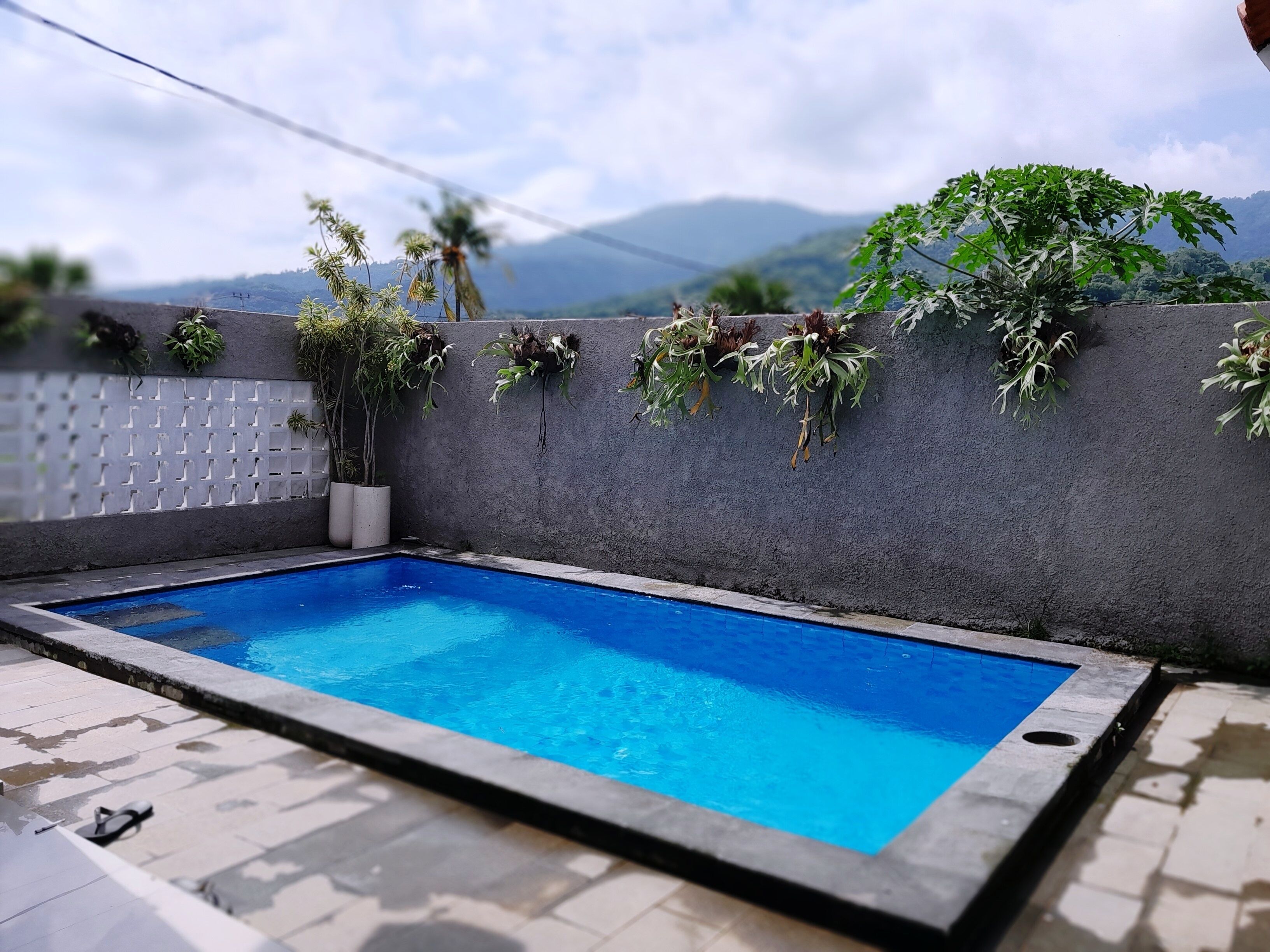 Una piscina rectangular con revestimiento azul, rodeada por una terraza de baldosas.