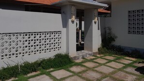 Un edificio residencial con techo de tejas, una pared decorativa con motivos circulares y un patio empedrado con césped.