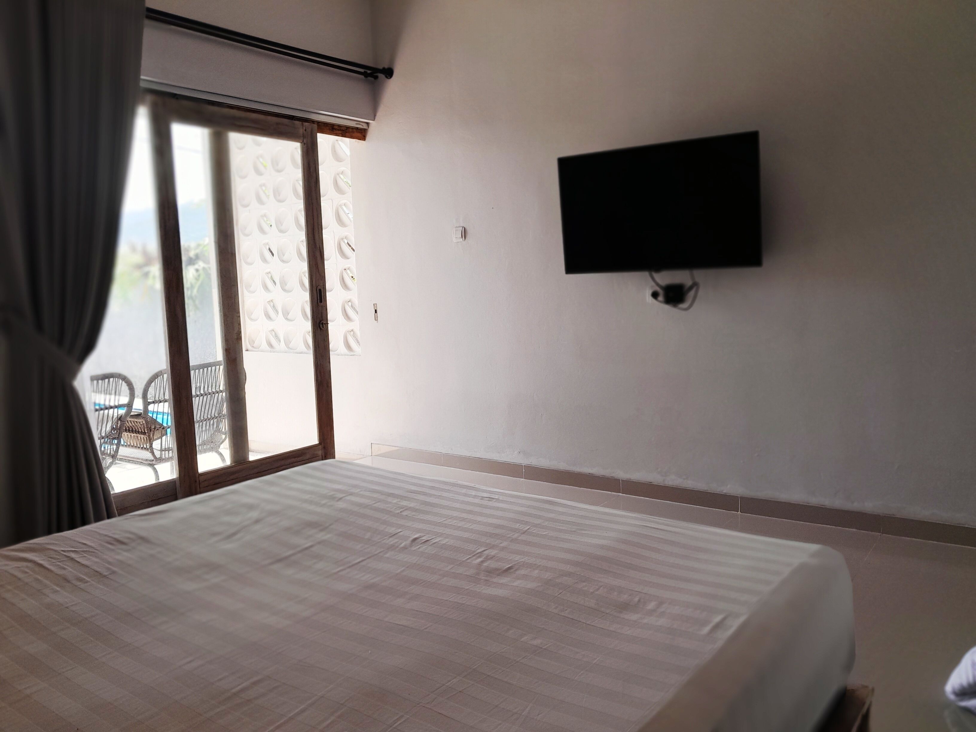 A hotel room with a bed, a TV mounted on the wall, and a sliding glass door leading to an outdoor area with chairs.