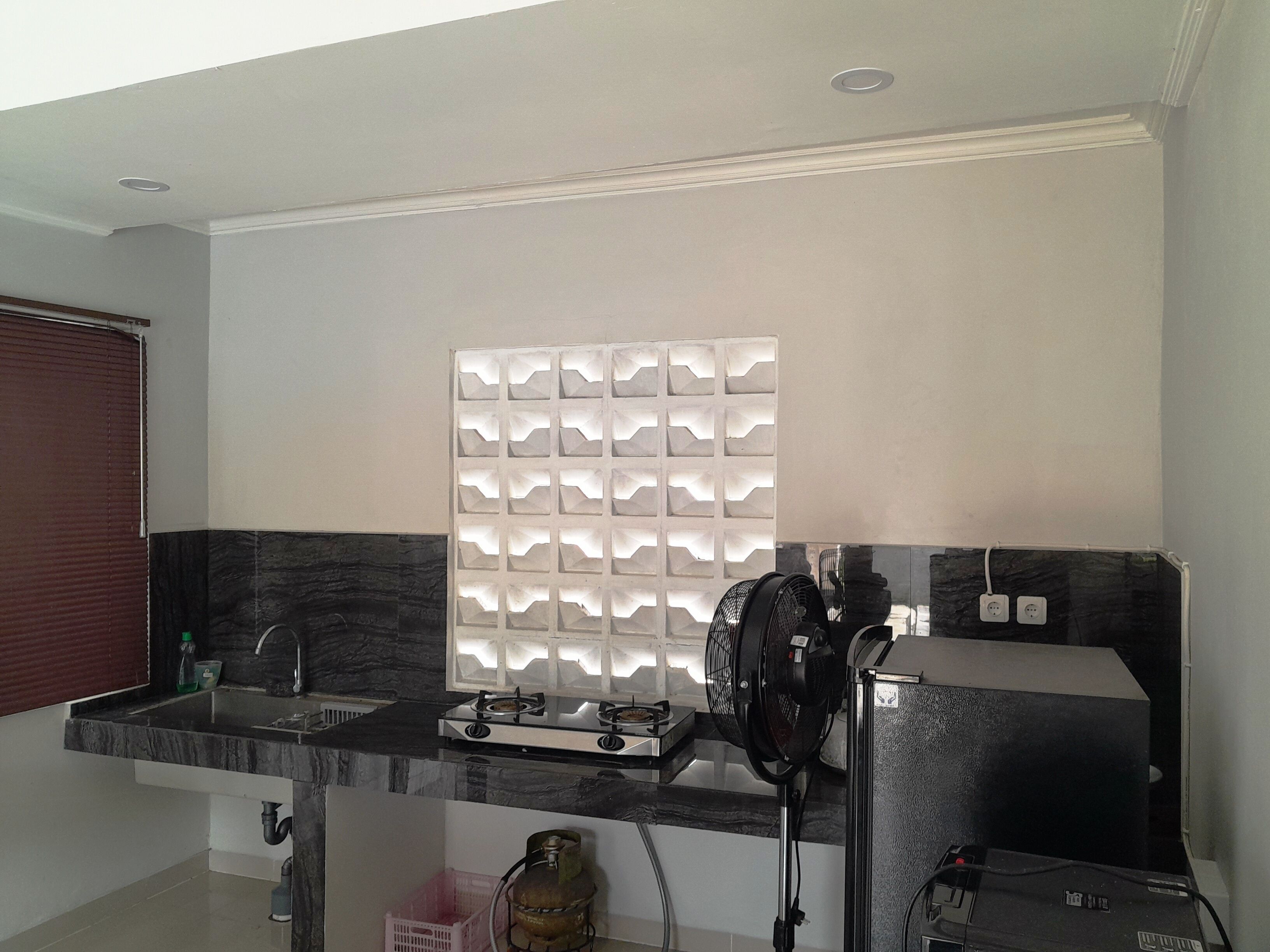 A kitchen with a gas stove, a sink, a fan, and a decorative light panel.