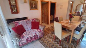 A living room with a sofa, a dining table with chairs, a clock, and a painting on the wall. - Holiday apartment with pool, Wi-Fi and terrace (Siófok)