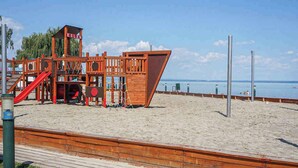 A wooden play structure with a slide and climbing area, adjacent to a sandy beach with a wooden boardwalk. - Holiday apartment with pool, Wi-Fi and terrace (Siófok)