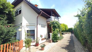 A two-story house with a balcony, a gravel driveway, and potted plants. - Holiday apartment with pool, Wi-Fi and terrace (Siófok)