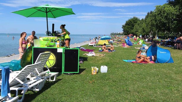 A beachside setting with lounge chairs, a green umbrella, and people relaxing. - Holiday apartment with pool, Wi-Fi and terrace (Siófok)