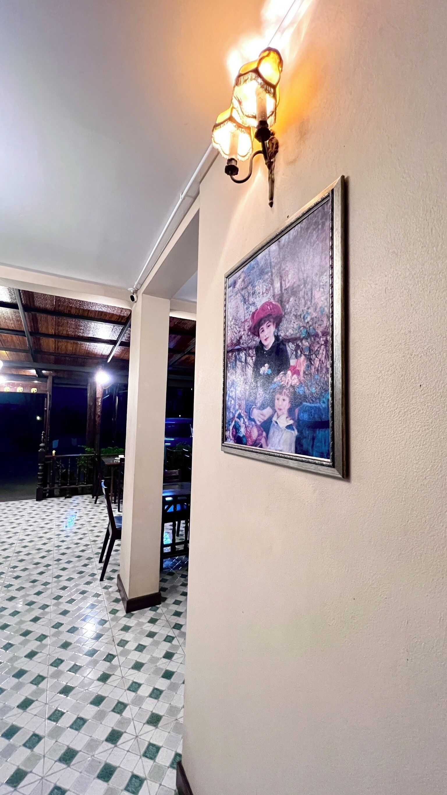 A hallway with a tiled floor, a framed painting on the wall, and a wall-mounted light fixture.