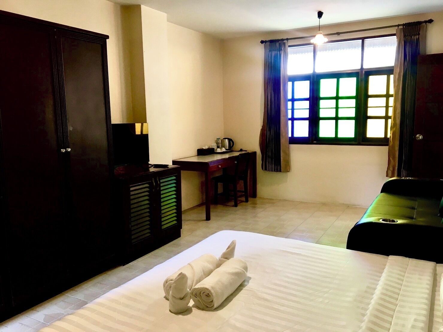 A hotel room with a bed, a desk, a chair, a TV, and a window with curtains.