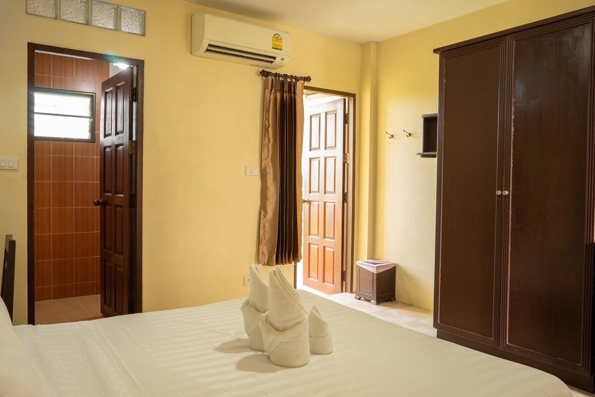 A hotel room with a bed, a wardrobe, a door, and an air conditioning unit.