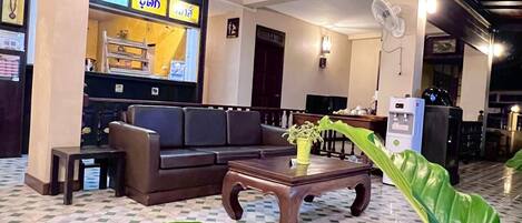 A hotel lobby with a checkered floor, a sofa, a coffee table, a potted plant, and a television.