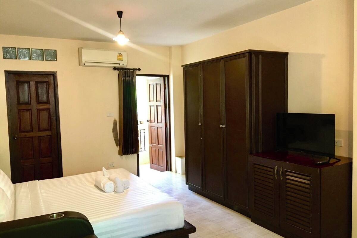 A hotel room with a bed, a wardrobe, a television, and an air conditioning unit.