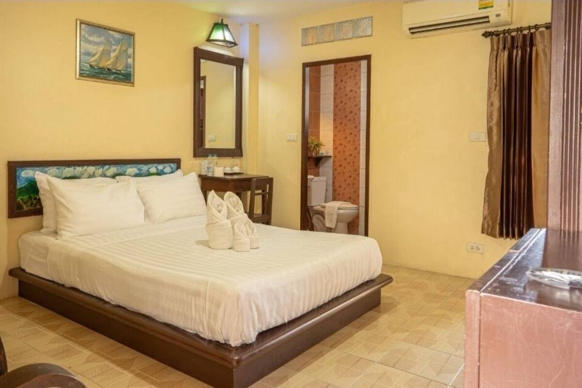 A hotel room with a bed, a desk, a chair, a painting, a mirror, and a bathroom door.