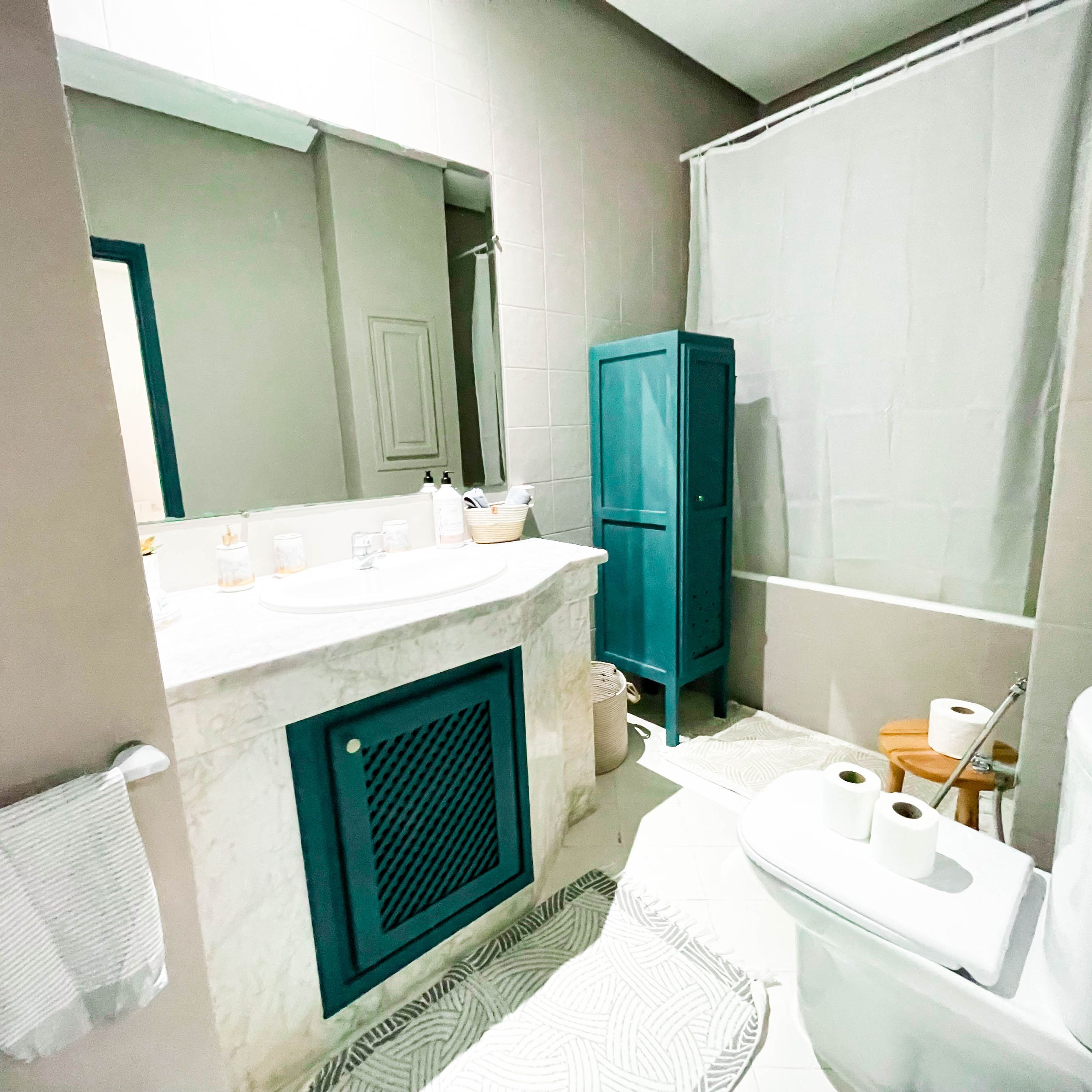 A bathroom with a marble sink, a blue cabinet, a shower curtain, and a toilet.