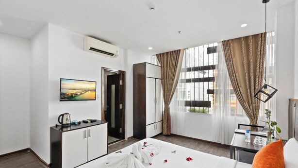 A hotel room with a bed, a desk, a chair, a TV, and a window with curtains.