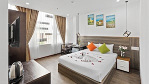 A hotel room with a bed, bedside tables, a desk, a chair, a television, and artwork on the wall.