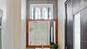 A bathroom with a shower, a sink, a mirror, and a dark door.