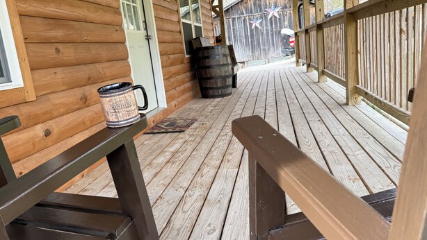 Une terrasse en bois avec un banc, un bâtiment de style rustique et un tonneau.