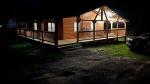 Une cabane en bois avec une véranda, des fenêtres et une voiture garée à proximité.