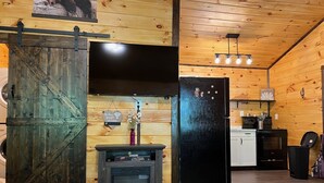 L’intérieur d’un chalet rustique, avec une porte en bois, un réfrigérateur noir, une cheminée et un coin cuisine.