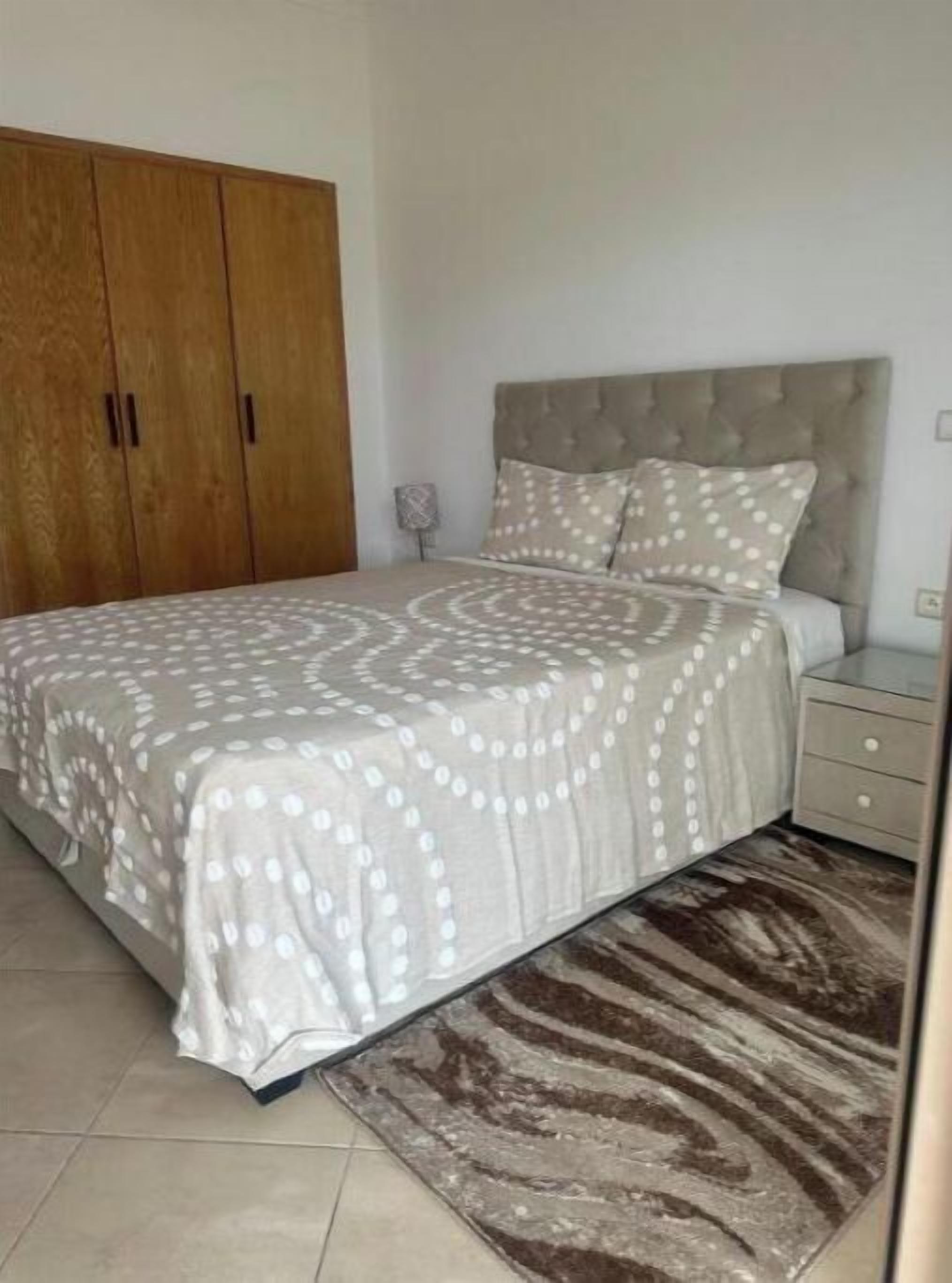 A bedroom with a bed, a nightstand, a wardrobe, and a patterned rug.