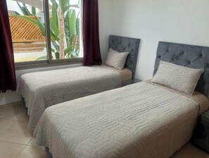 Ein Schlafzimmer mit zwei Einzelbetten, einem Fenster mit Vorhängen und Blick auf Grün.