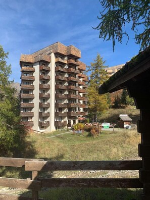 A multi-story building with balconies, surrounded by trees and a grassy area.