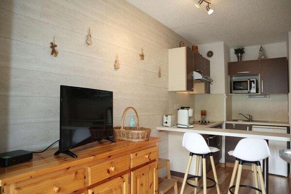 A modern kitchen with wooden cabinets, a built-in microwave, and a TV on a wooden stand.