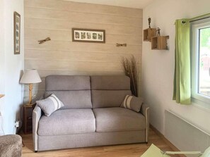 A neutral-toned sofa with a cushion, a small table with a lamp, and a window with a green curtain.
