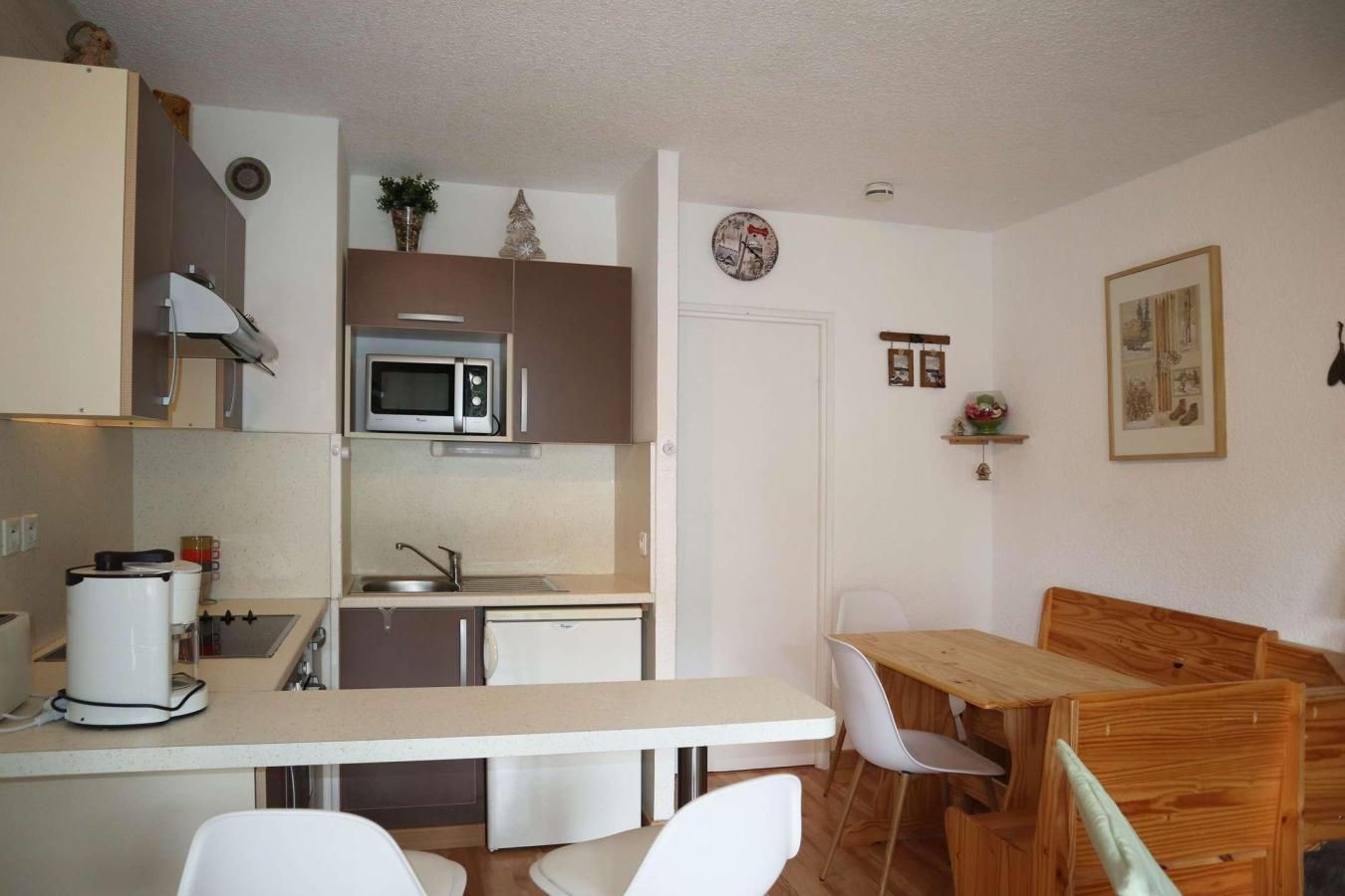Cocina compacta con microondas, pileta y pequeño refrigerador. Hay un comedor con mesa y sillas de madera.