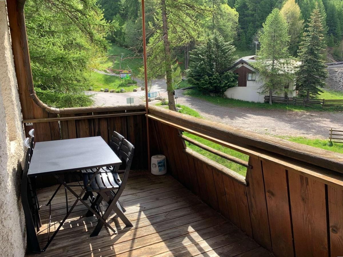A wooden deck with a table and chairs, overlooking a road and greenery.