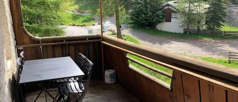 A wooden deck with a table and chairs, overlooking a road and greenery.