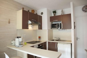 Eine kleine Küchenzeile mit Herd, Mikrowelle, Spüle und kleinem Kühlschrank.